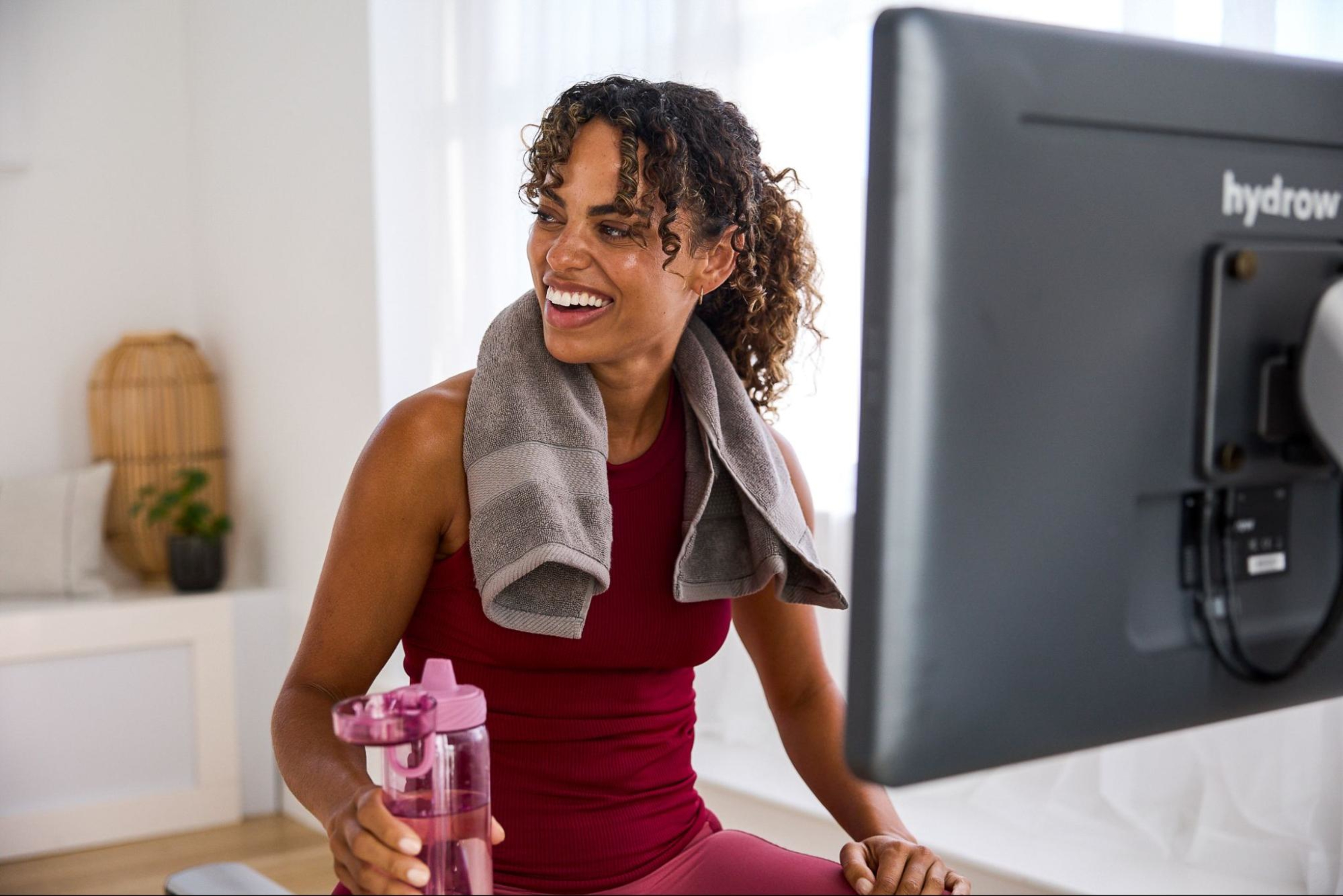 Woman smiles and drinks water after working out on a Hydrow Origin rowing machine.
