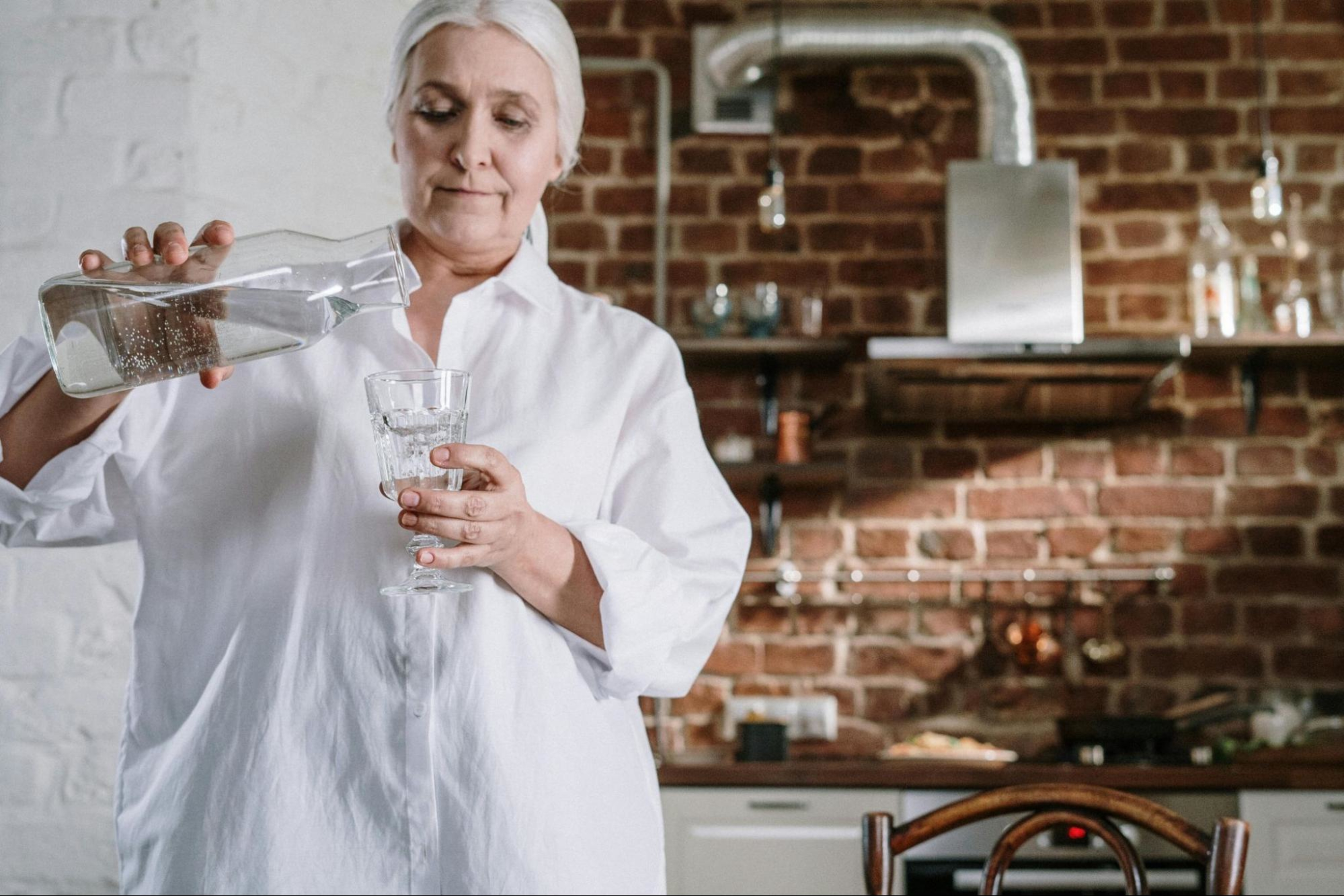 Aging woman pours a glass of water to focus on her nutrition as she ages.