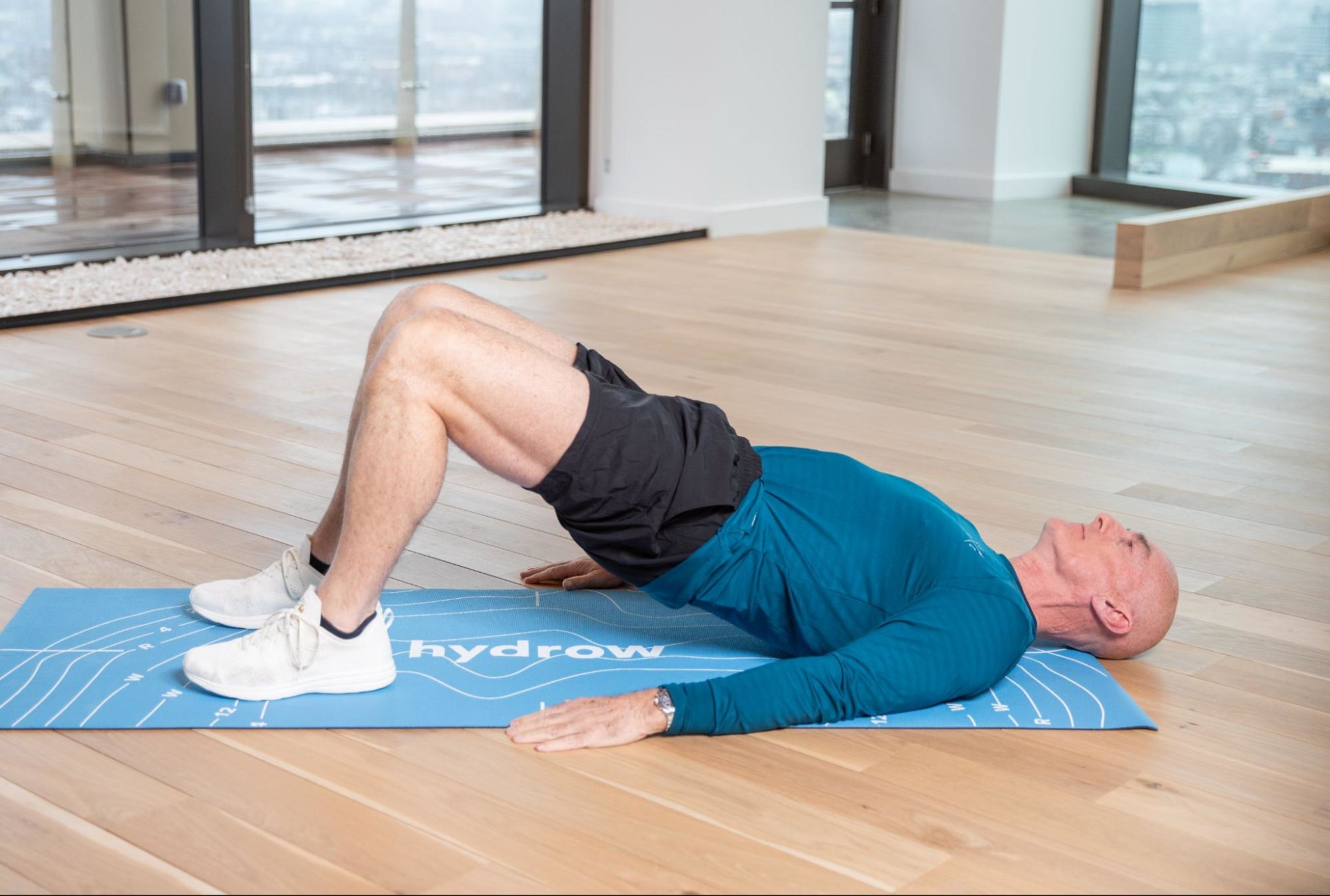 Hydrow Athlete Pete demonstrates how to do a glute bridge, a popular type of strength training workout for marathoners.
