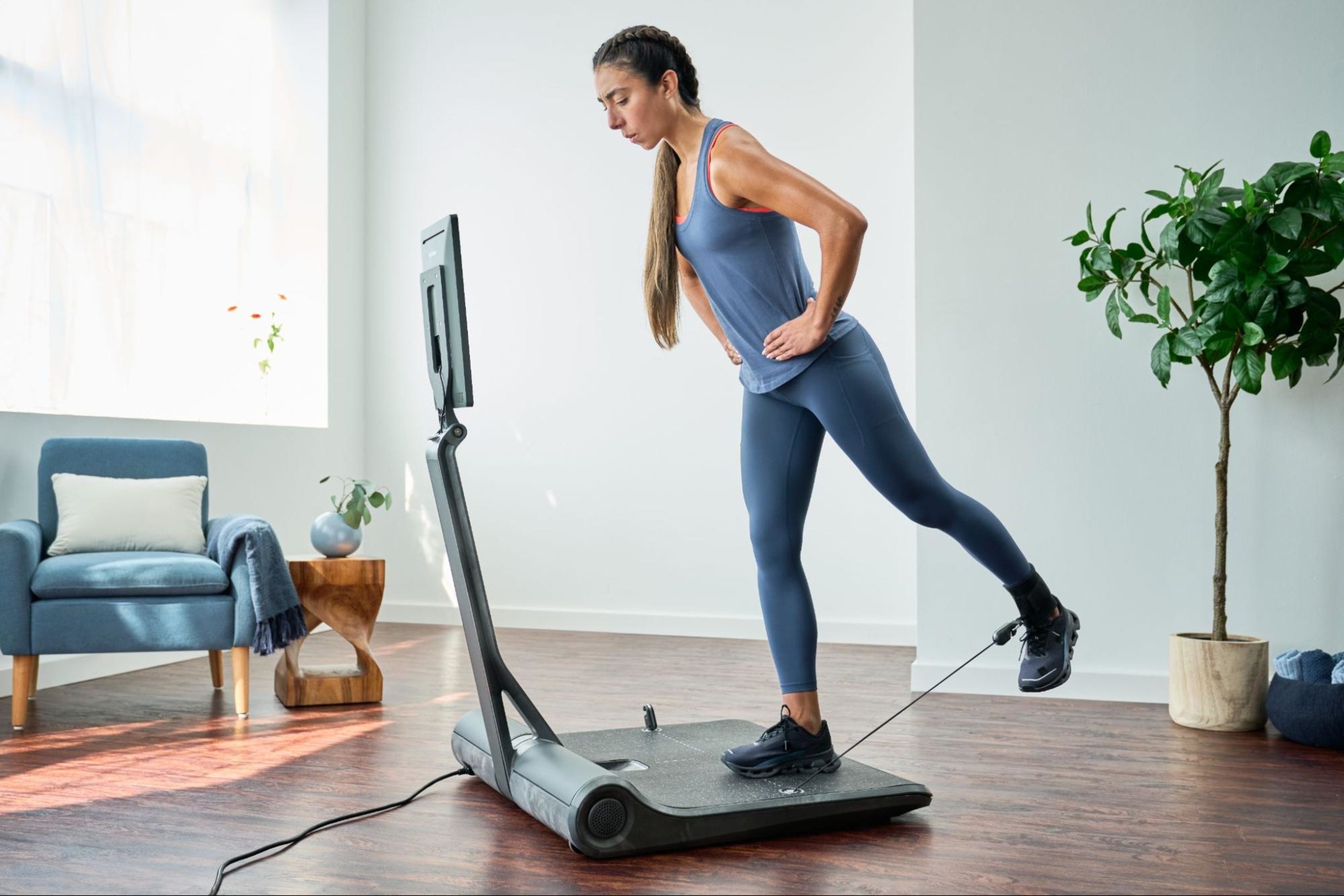 Woman does a strength workout on her LYQUID using the ankle strap accessory.