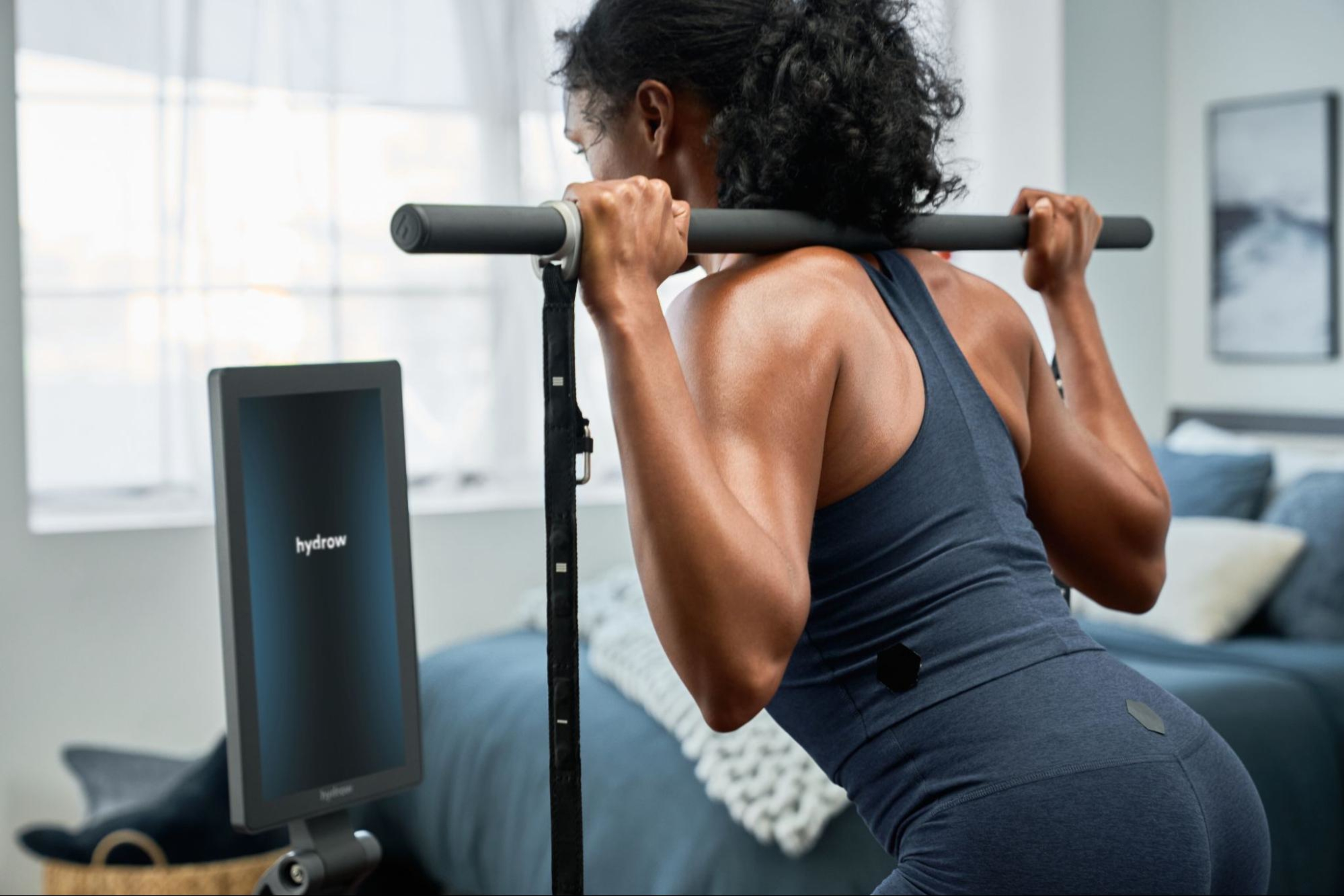Man does a workout on her LYQUID strength machine using the barbell accessory.