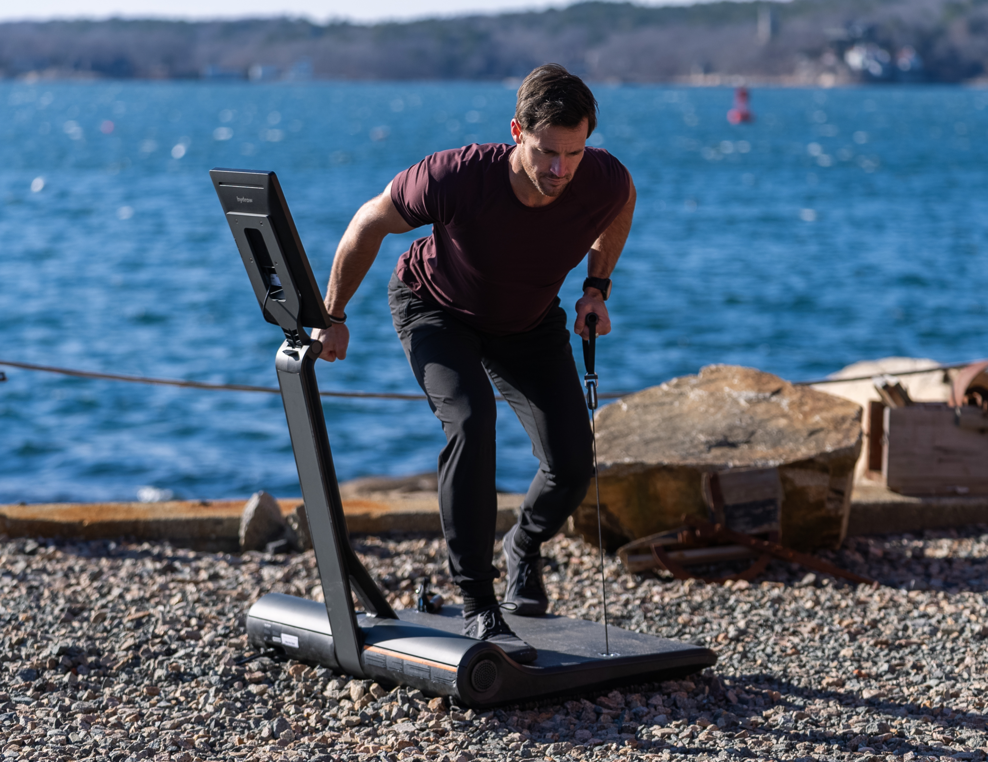 Hydrow Athlete Lance Parker does a single arm bent over row (staggered) on a LYQUID strength machine outdoors.