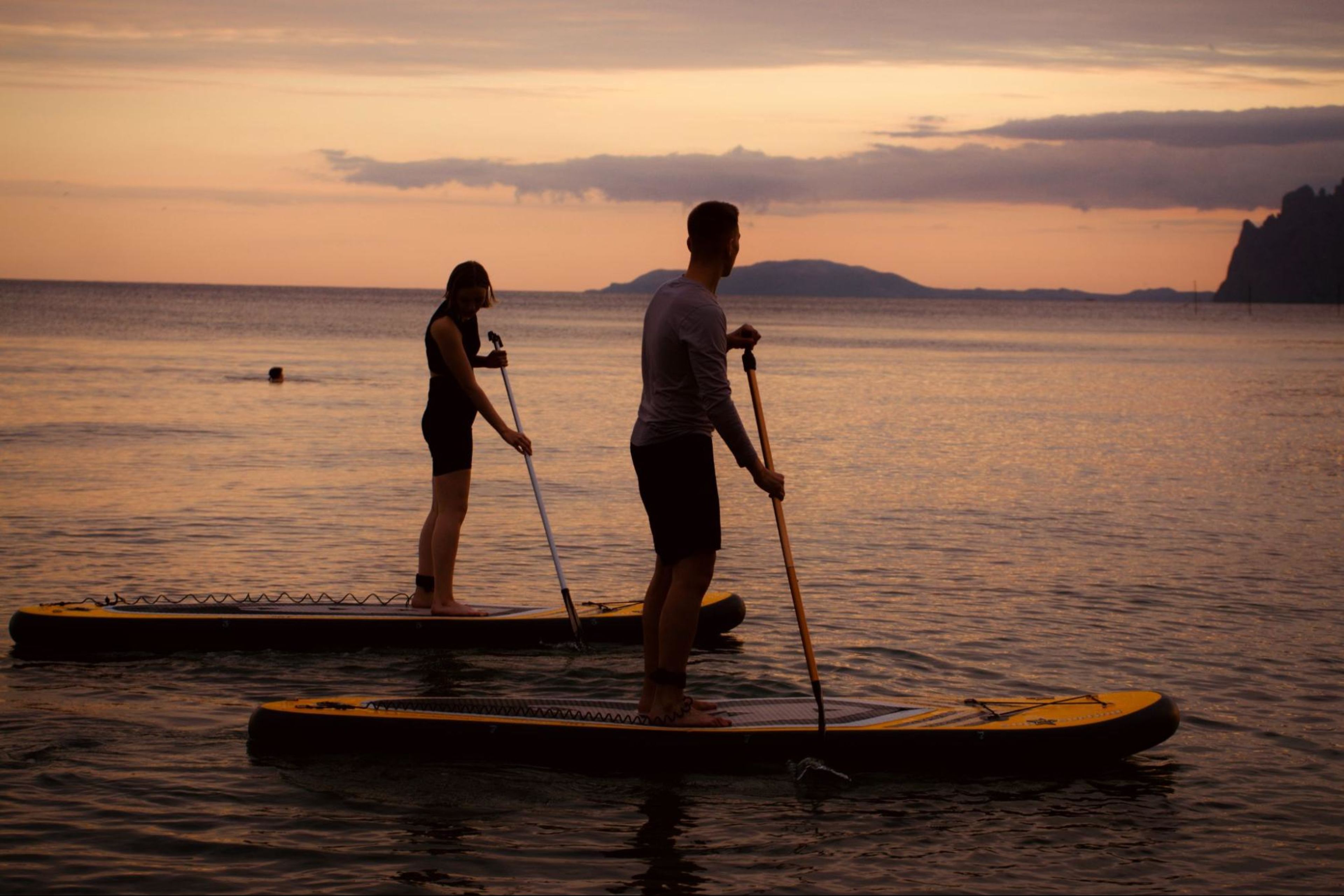 A man and a woman work out on vacation by paddleboarding on the ocean.