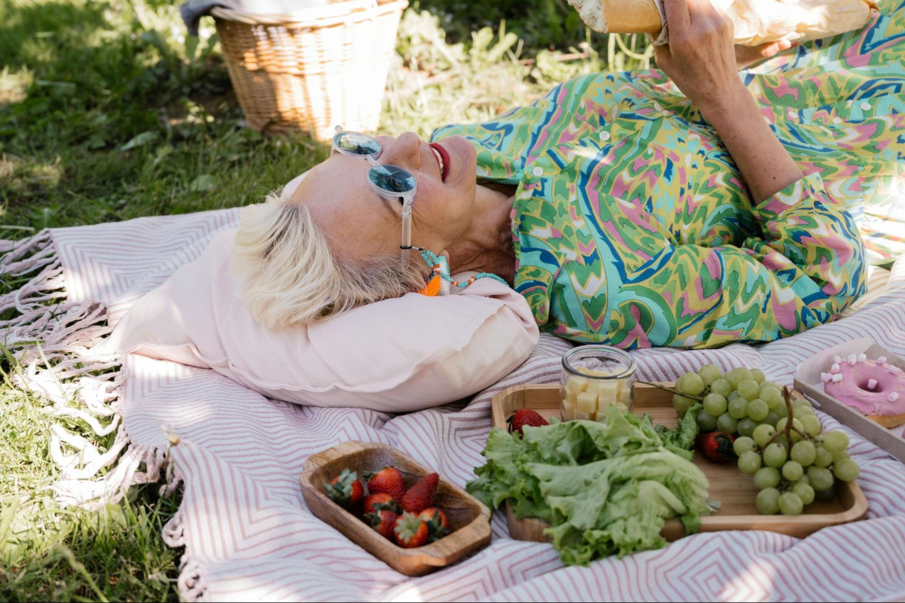 Old woman lays on a picnic blanket with strawberries, grapes, bread, and cheese to demonstrate the difference between healthspan and lifespan.