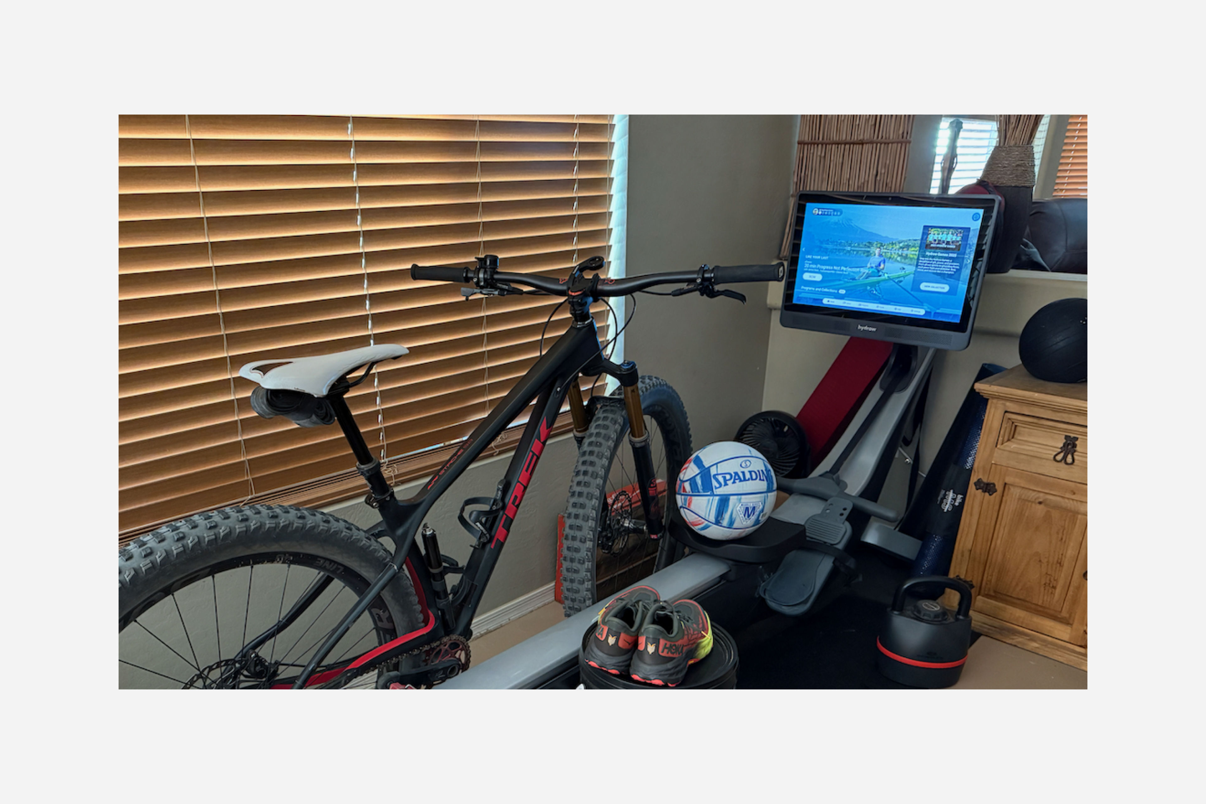 A Hydrow Member's at-home rowing machine setup, including a Hydrow rower, bike, basketball, and sneakers.