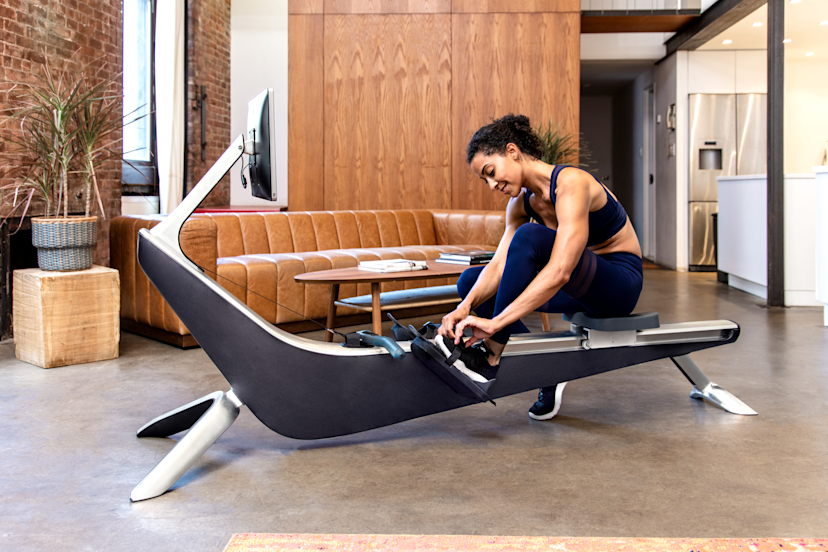 Woman uses a Hydrow rowing machine after considering the pros and cons of rowing
