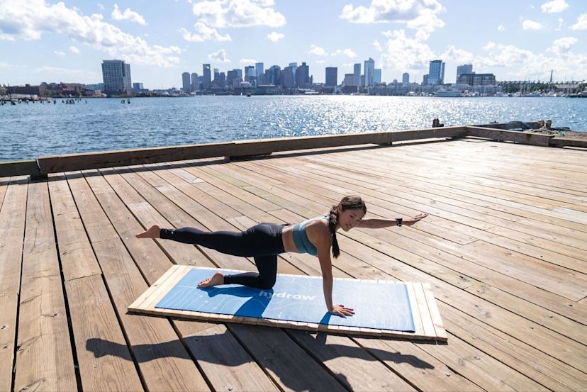 Hydrow Athlete does Pilates workout on a mat on the Boston waterfront.