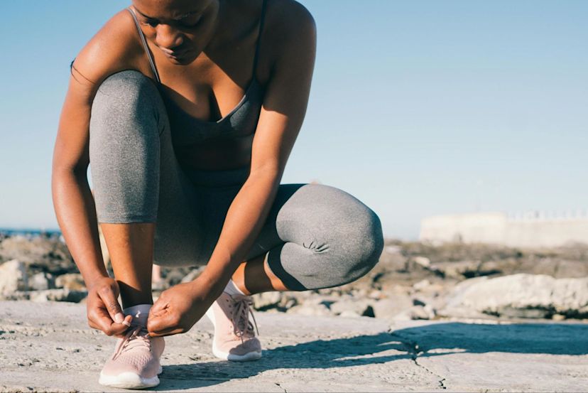 Woman ties her shoe to prepare to work out as she weighs cardio vs. strength training.