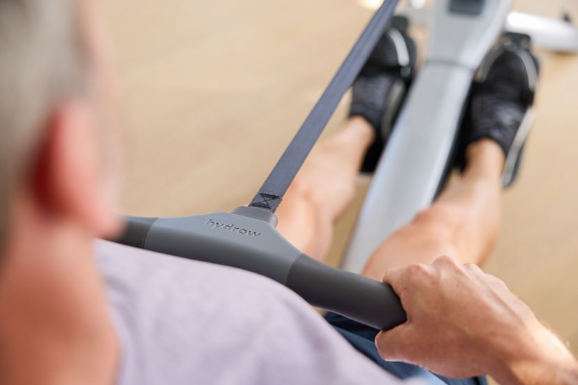 Man works out on a rowing machine wearing flat sneakers, the best shoes for rowing.