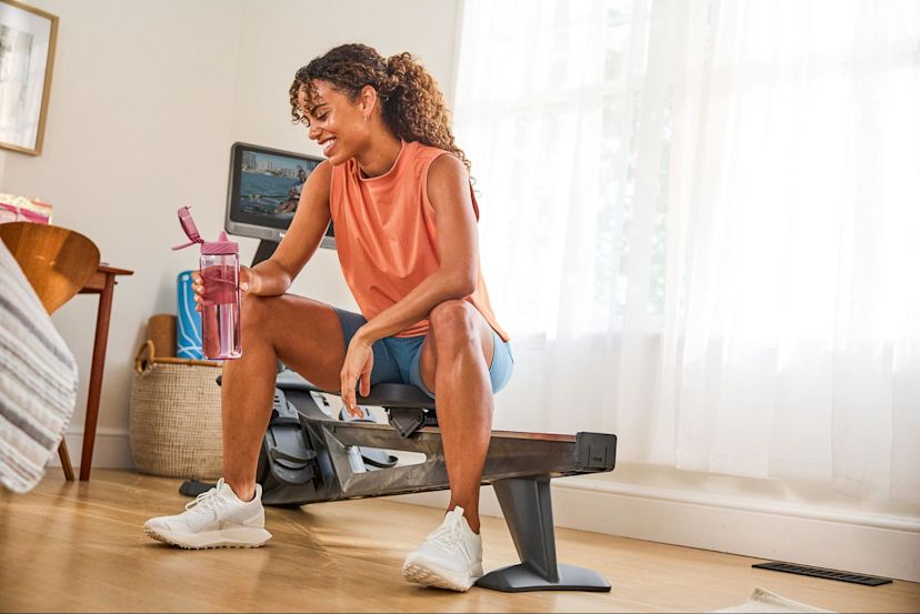 Woman drinks water after rowing on a Hydrow rowing machine after weighing a Hydrow vs. Rogue Echo rower.