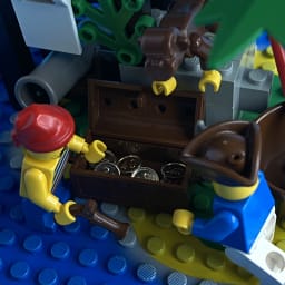 Two LEGO pirates and a monkey lean over gold coins in an open treasure chest