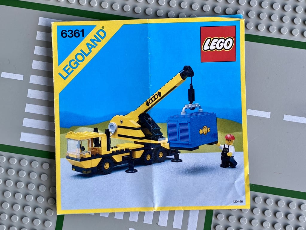 LEGO instruction booklet cover depicting a mining wearing a hard hat operating a mobile crane holding a container suspended above ground