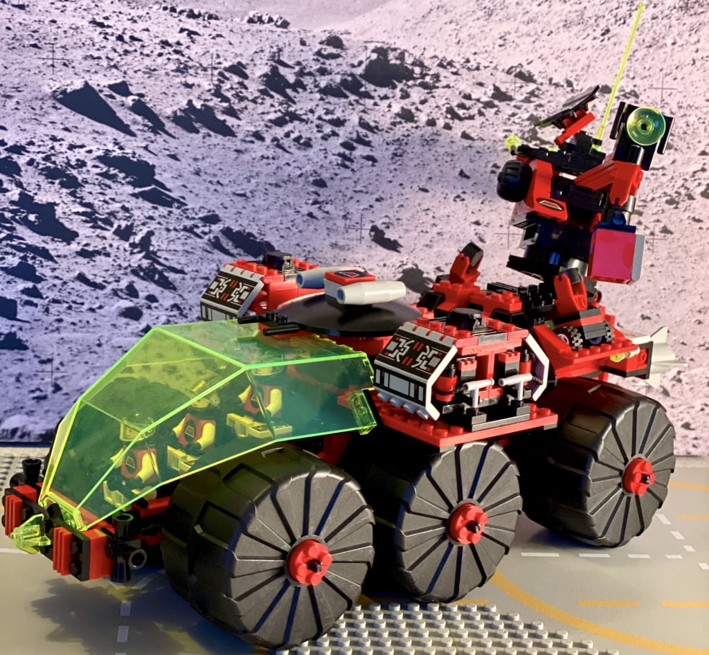 The finished Mega Core Magnetiser against a moon surface background, with all three minifigs in the cockpit and the crane lifting the small container
