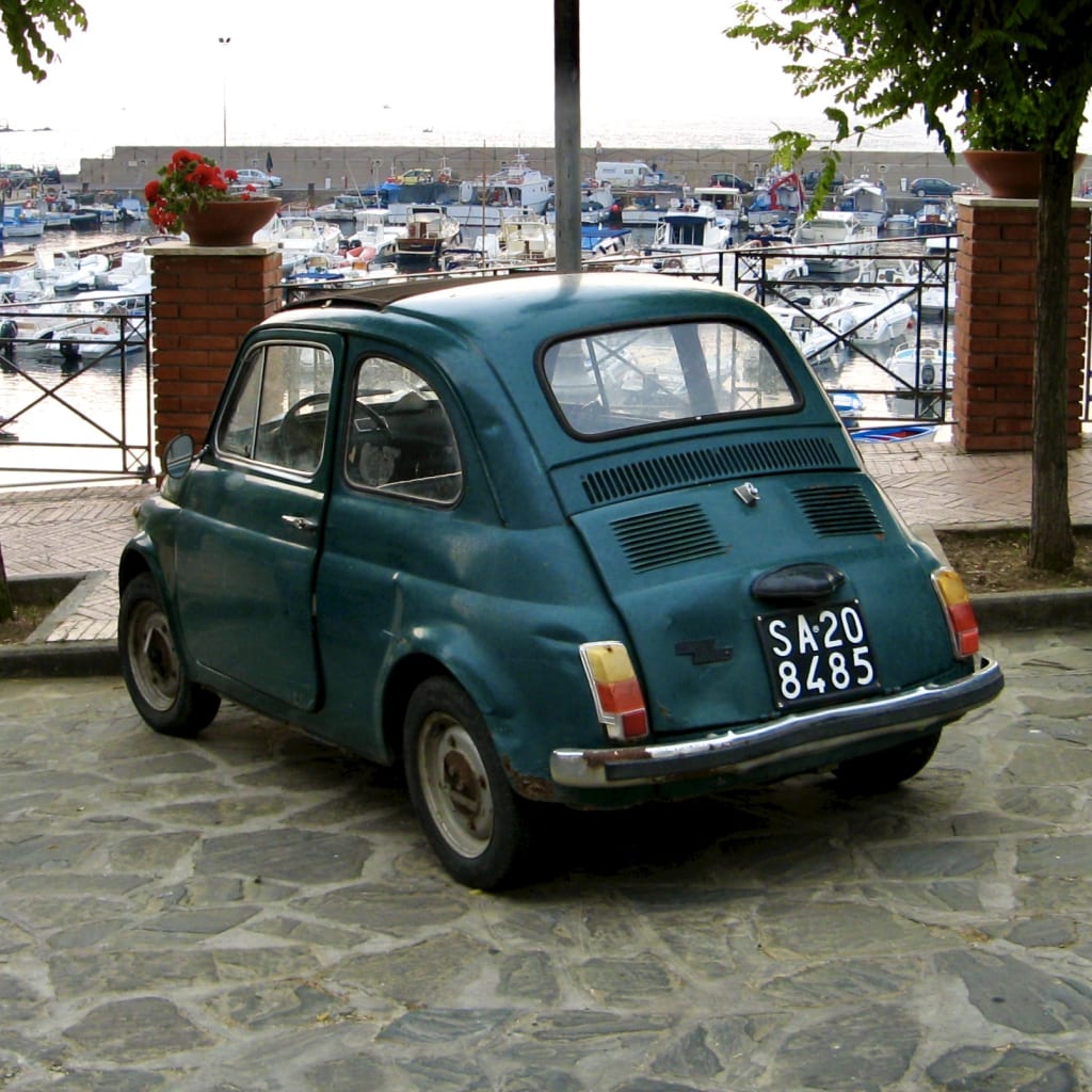 A Fiat 500 parked in front of the quays of an Italian village