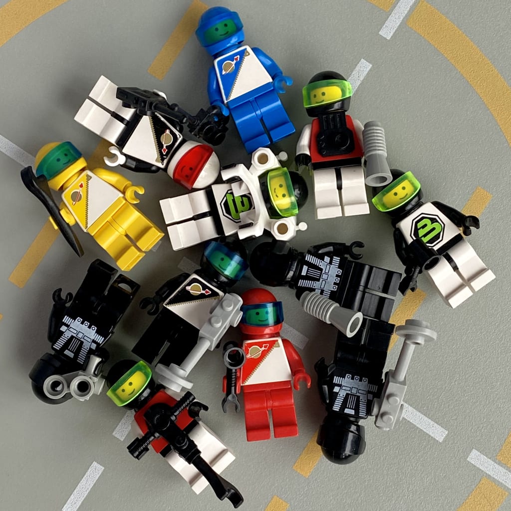 12 space minifigures laying on their backs on a LEGO baseplate