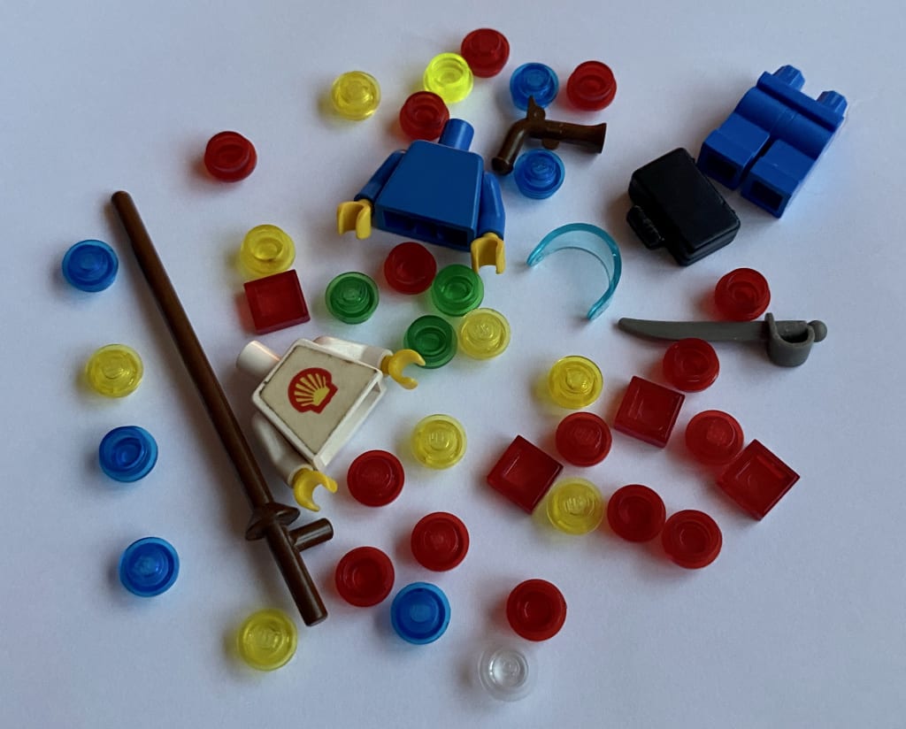 A pile of LEGO pieces, mostly transparent 1x1 plates, a couple of minifig torsos and some minifig accessories.
