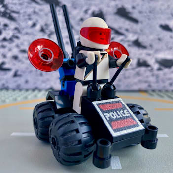 A tiny 4-wheeled LEGO space police vehicle with a standing minifigure operating the vehicle using two levers.