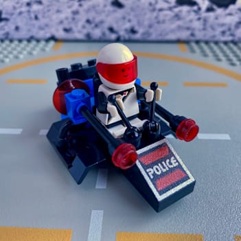 A small flying LEGO space police vehicle with a sitting minifigure operating the vehicle using two levers.