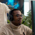 Person wearing headphones and turtleneck sits at a desktop computer.