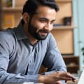 Person in gray button-down shirt works on laptop.