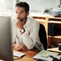 A businessperson sits at a desktop computer and considers the business challenges facing their organization.