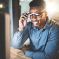 An employee at their desk in an office setting, smiling at their desktop monitor as if talking on a video call.