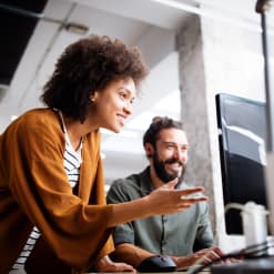 Two coworkers collaborate on a desktop computer. 