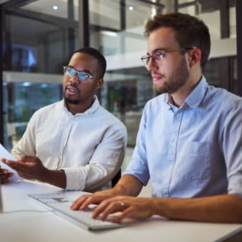 Two young professionals collaborate at a desktop computer.