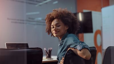 Person sits in conference room, turned around in seat and smiles at camera.