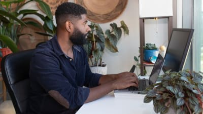 Person sits at desktop computer with houseplants on desk.