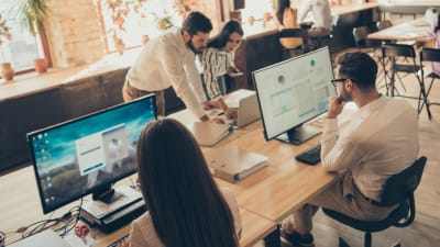 Group of young professionals work and collaborate on desktop computers in an open office.