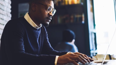 Person in navy blue sweater uses a laptop computer in an office.