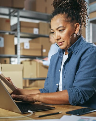 Person works on a laptop in a retail warehouse with cardboard boxes.