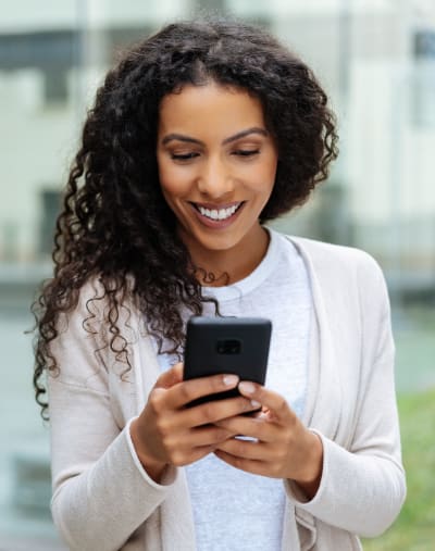 A person holds their cell phone in their hands and gets work done while walking outside.