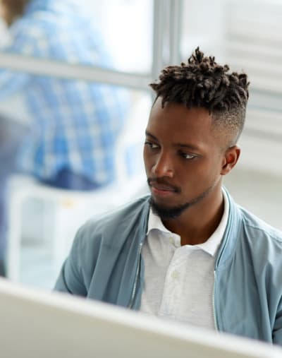 An employee looks across the room and sits in front of a desktop computer.