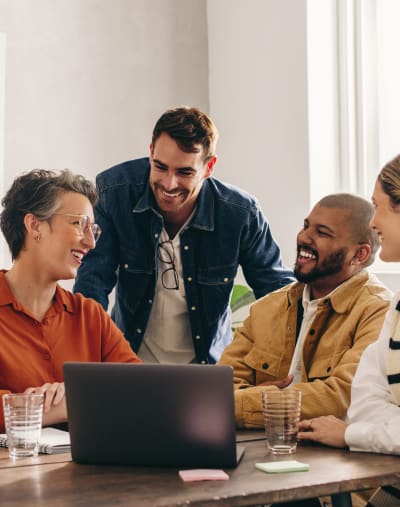 Four co-workers huddle around a business laptop and smile, enjoying the efficiency of their digital asset management platform.