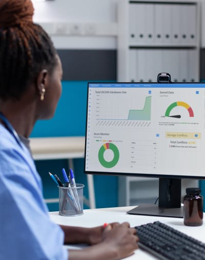 A healthcare professional reviews a reporting dashboard on a desktop computer.