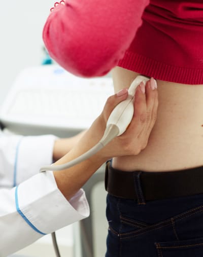 A healthcare professional uses an ultrasound device on a patient’s left side.