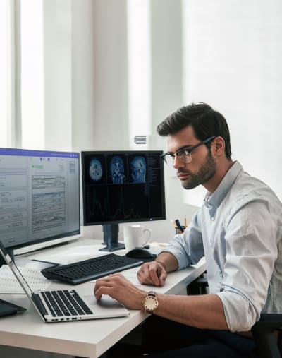 Healthcare worker checks laptop while processing electronic documents.