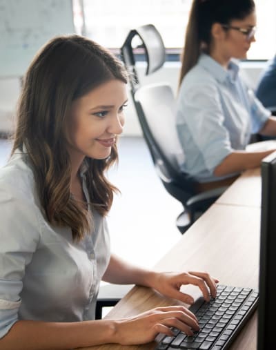 Two people sit and type on computer keyboards in an office setting.