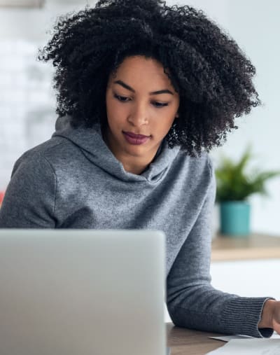 Person sits and looks at a laptop. There are papers on the table.