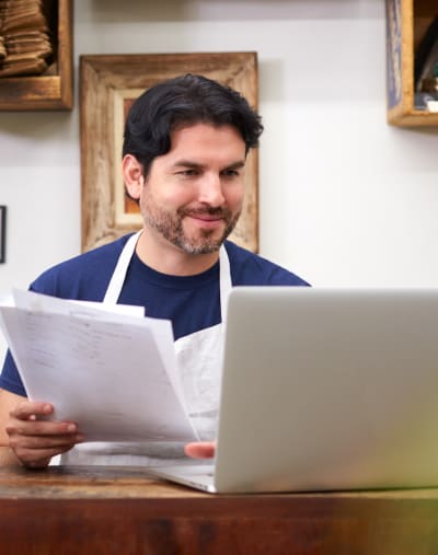 Person sorts through paperwork while looking at a laptop.