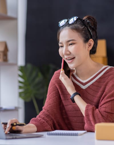 Person holding a pen talks on a mobile phone and looks at information on a laptop.