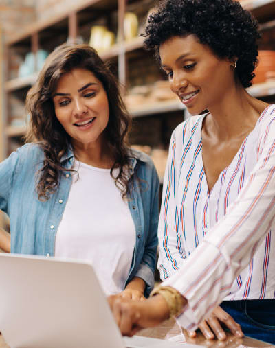 Two workers smile and look at information on a laptop.