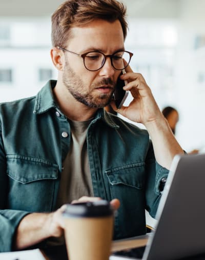 Person in glasses, using a mobile phone and looking at a laptop preparing to submit financial aid applications.