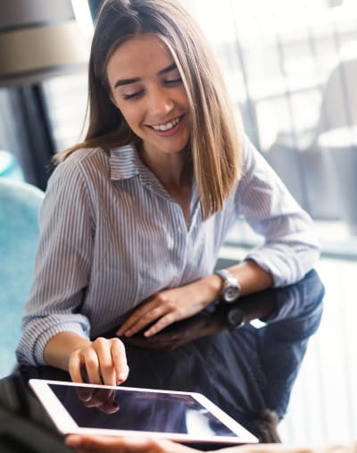 Two people sitting at a table while one shows the other a tablet computer.