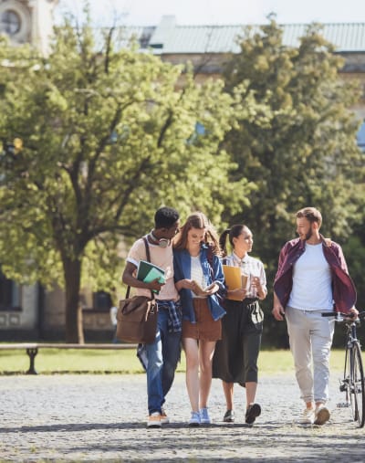 Four college students walking on campus at their higher education institution.