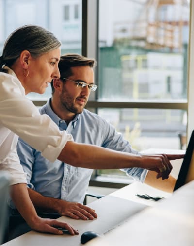 Two people look at a computer screen in an office setting.  