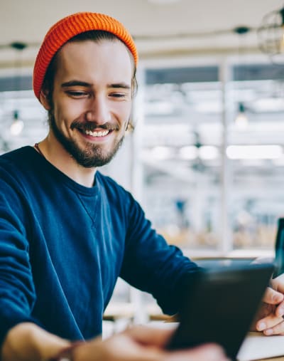 Person wearing a winter hat sits at a table and looks at a mobile phone. 