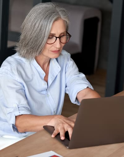 A person wearing glasses sits and types on a laptop. There is a notebook on the table.